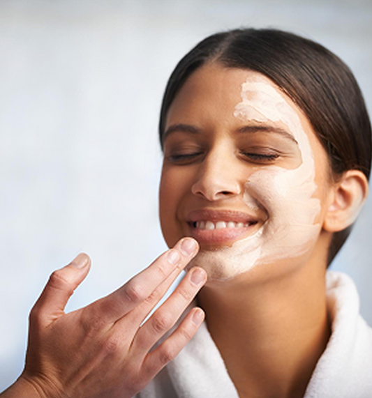 A smiling woman enjoys a facial treatment as a hand gently applies cream to her face, highlighting skincare and relaxation