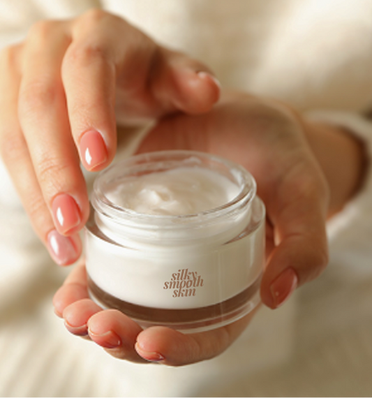 Hands holding a jar of silky smooth skin cream, with fingers poised to apply the moisturizing lotion